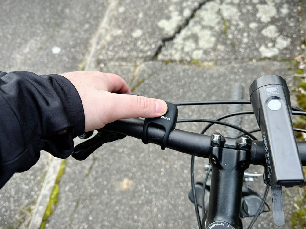 Eine Hand betätigt die Rockbros-Fahrradklingel am Lenker eines Fahrrads. Der Druckmechanismus ist gut sichtbar.