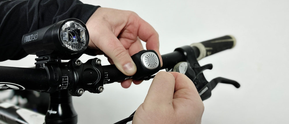 Eine Person montiert die Rockbros-Fahrradklingel an den Lenker eines Fahrrads. Die flexible Halterung wird befestigt.