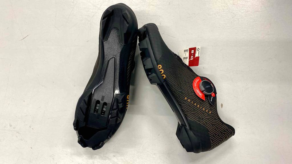MTB-Schuhe für Herren im Test: Ein Paar MTB-Schuhe, ein Schuh auf der Seite liegend einer mit Sohle nach oben auf einer hellen Fläche.
