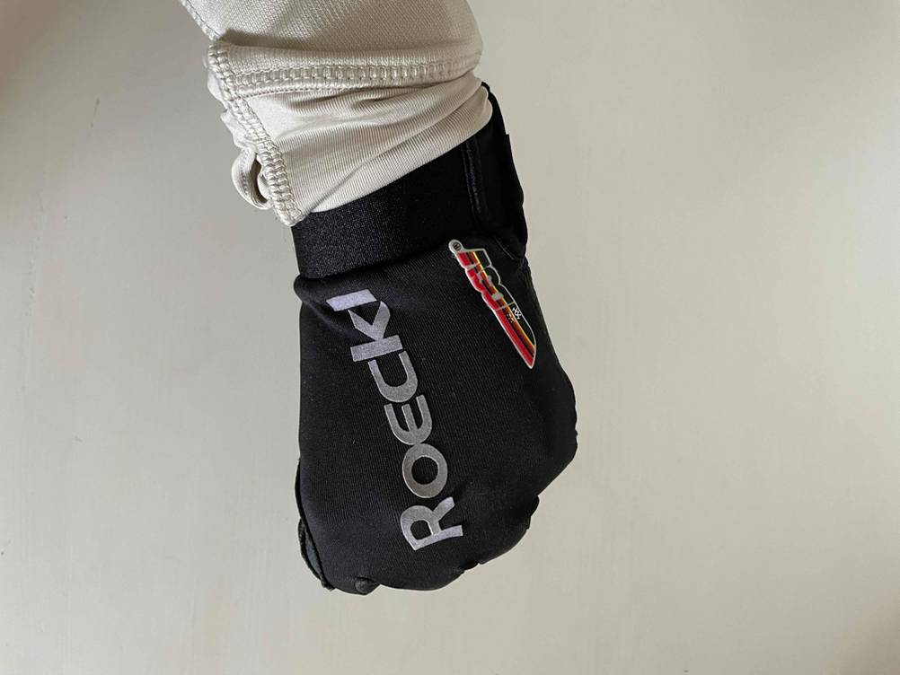 Laufhandschuhe getestet: Hand macht mit einem angezogenen Handschuh eine Faust vor einer weißen Wand.