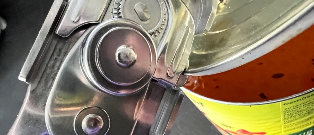 Dosenöffner-Zange hebt einen Deckel einer Dose hoch.
