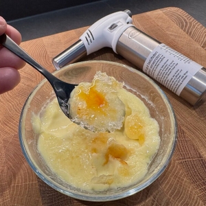 Auf einem Löffel vor dem Rösle-Flambierbrenner liegt Crème Brûlée