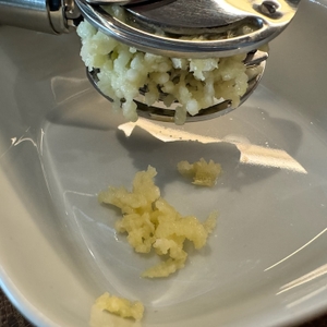 Gepresster Knoblauch fällt aus der Presse in eine Schale.