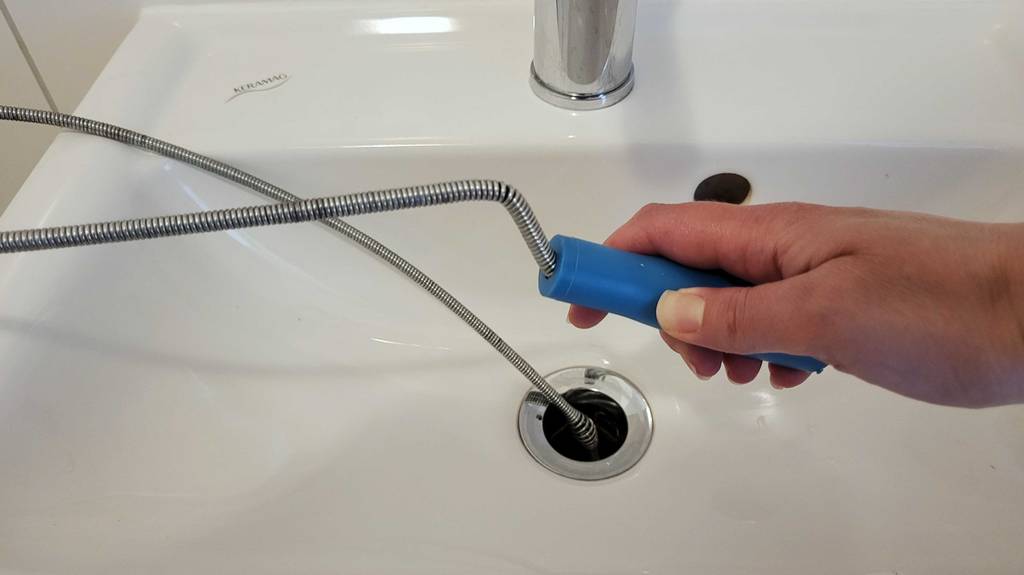 Im Test: Eine Hand führt eine Rohrreinigungsspirale in den Abfluss eines Waschbeckens ein.
