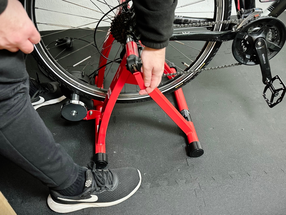 Ein Fahrrad wird mithilfe des Schnellspanners in den Rollentrainer von Sportneer eingespannt.