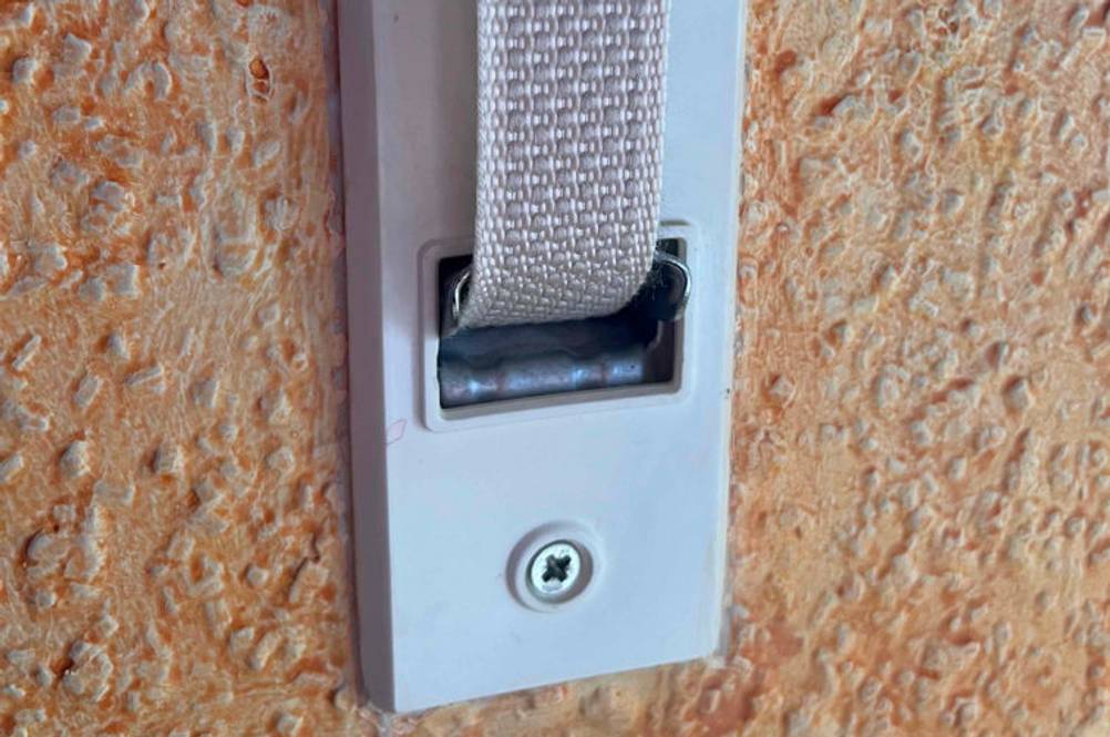 Weißer, getesteter Rollladengurt ragt aus der Wandhalterung, die sich auf einer orangen Wand befindet.