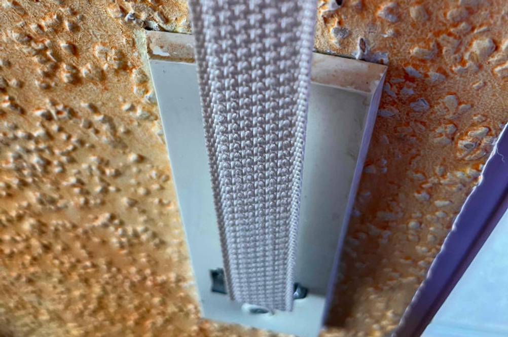 Rollladengurt im Test: weißer Rollladengurt inklusive Wandhalterung auf einer orangen Wand.