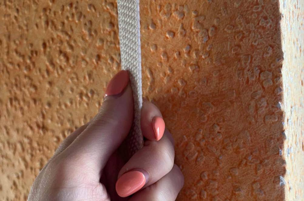 Rollladengurt-Test: Hand hält einen weißen Rollladengurt vor einer orangen Wand.