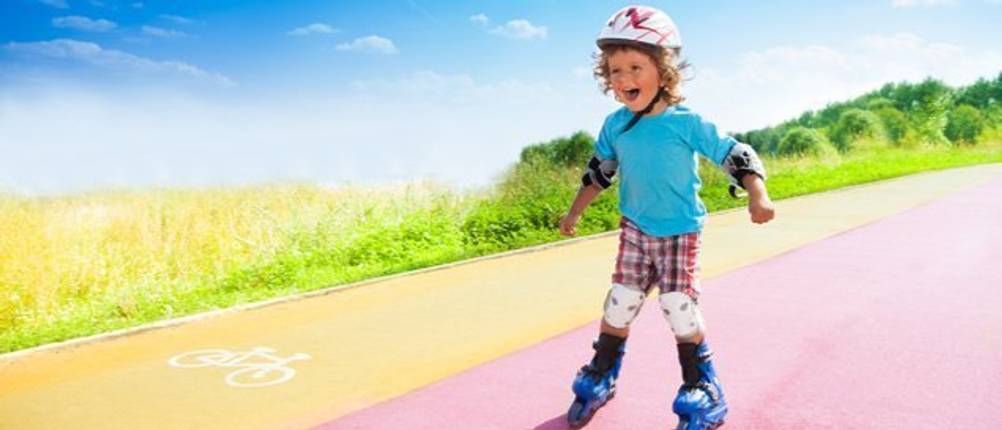 Kind lernt Rollschuhfahren auf einer Asphaltstraße neben einem Feld