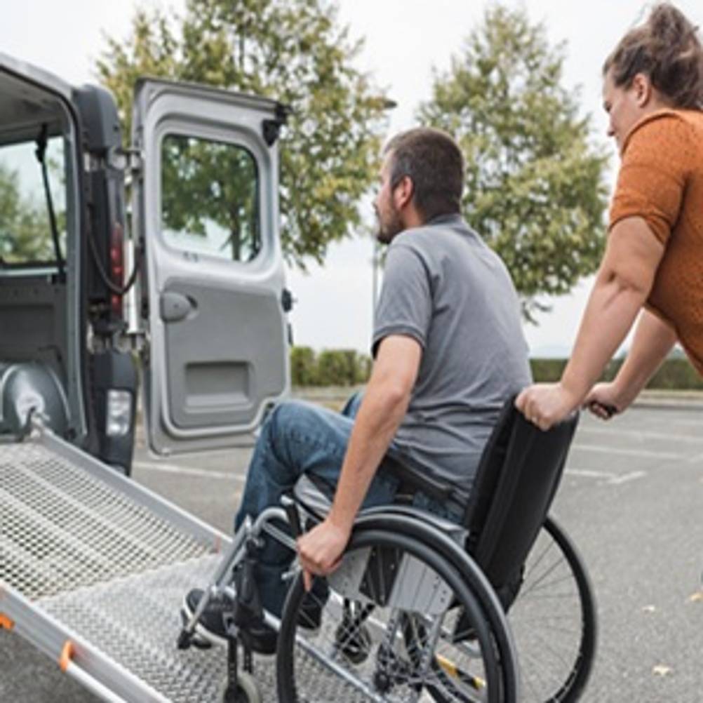 Rollstuhlrampe im Test: Frau schiebt Mann in Rollstuhl über eine Rampe ins Auto