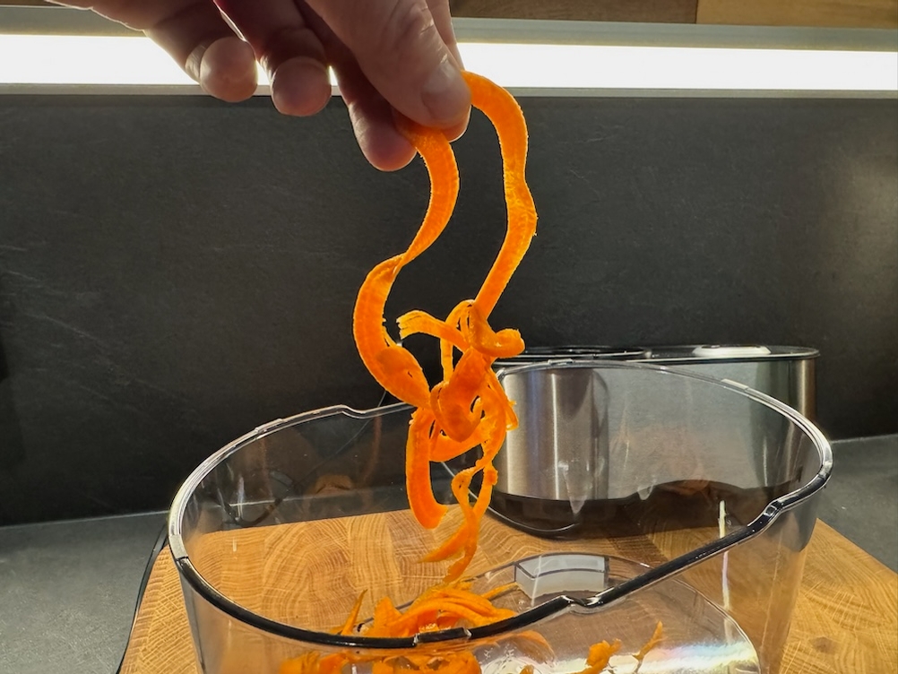 Eine lange Karottenspirale wird aus einem durchsichtigen Behälter in die Höhe gehoben.
