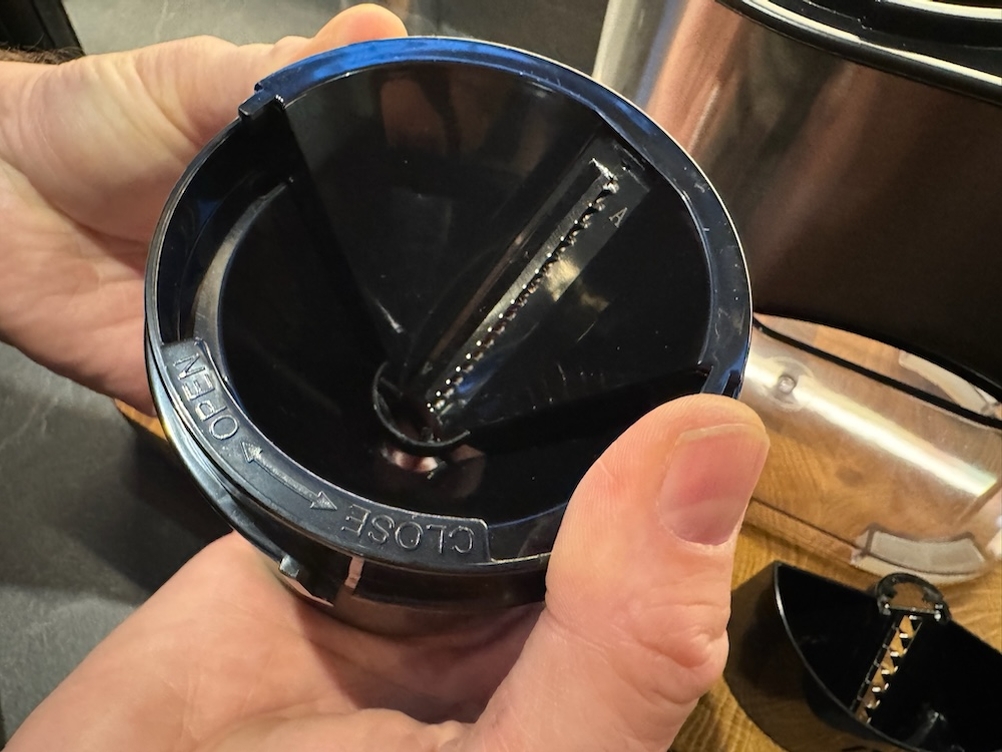 Eine Hand hält einen Schneidaufsatz und zeigt die Einfüllöffnung zur Kamera.