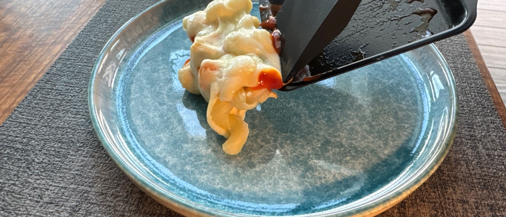 Mit Käse überbackene Nudeln werden mit einem Spachtel aus einer Pfanne des Rommelsbacher RC 1600 geschoben.