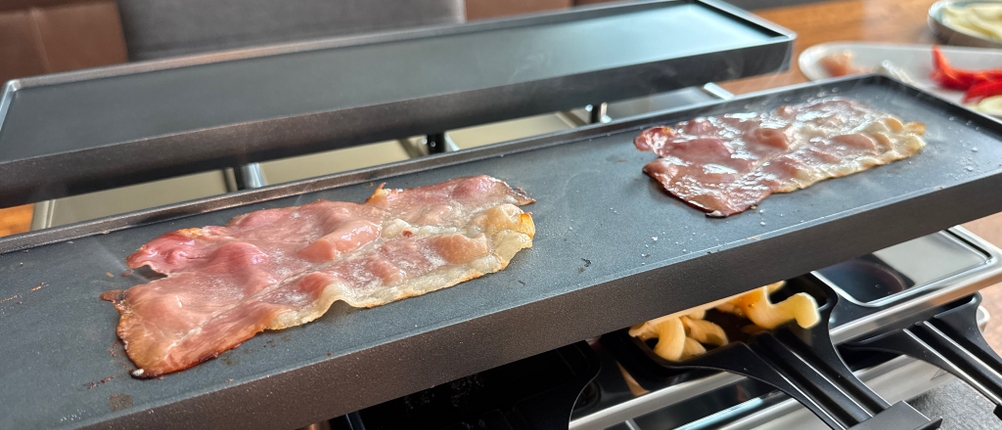 Auf der Grillplatte des Rommelsbacher RC 1600 liegen zwei Scheiben Speck.