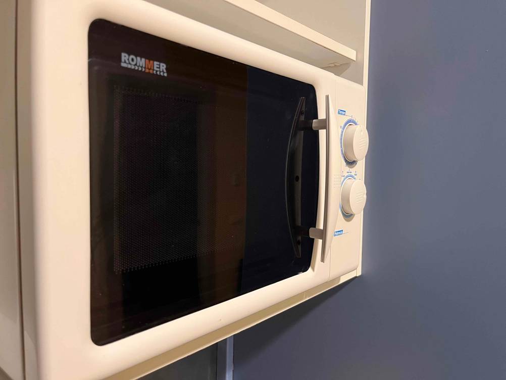 Weiße Rommer Mikrowelle ohne Grill im Test: Ansicht über Eck des in einem Hängeregal positionierten Geräts mit abgedunkelter Glasscheibe.