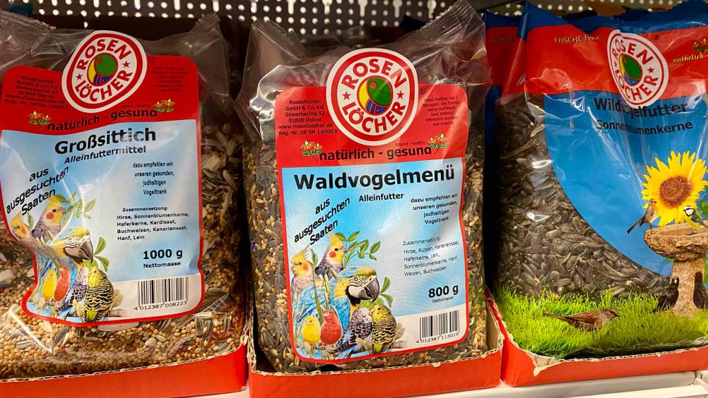 Im Test: Mehrere verschiedene Sorten Vogelfutter von Rosen Löcher stehen nebeneinander in einem Regal.