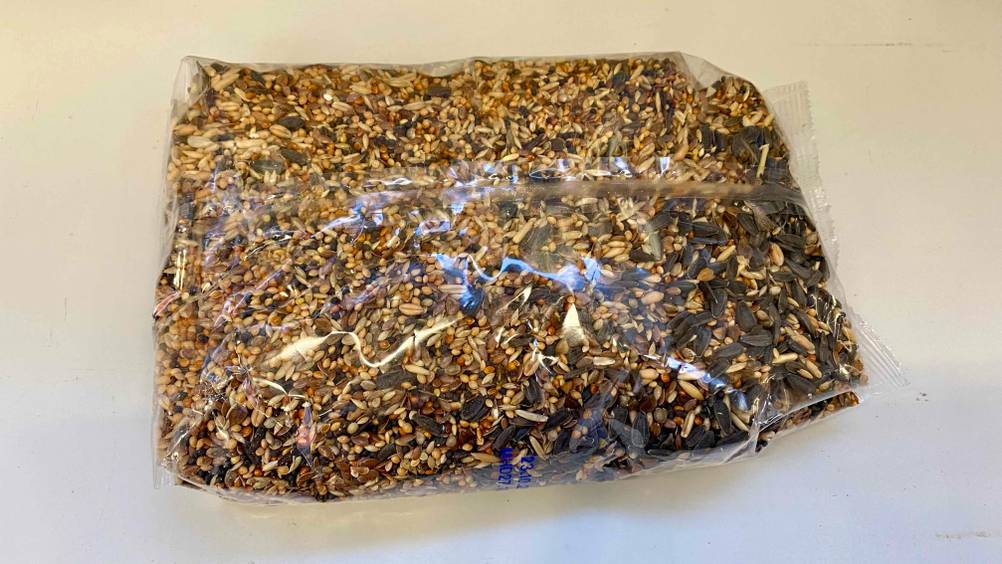 Eine Packung Vogelfutter liegt verpackt zum testen auf einer weißen Fläche.