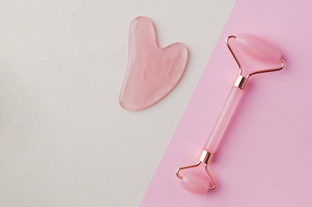 Rosenquarz-Roller-Test: Auf einem Tisch liegt ein Gua-Sha-Stein und ein Rosenquarz-Roller. 