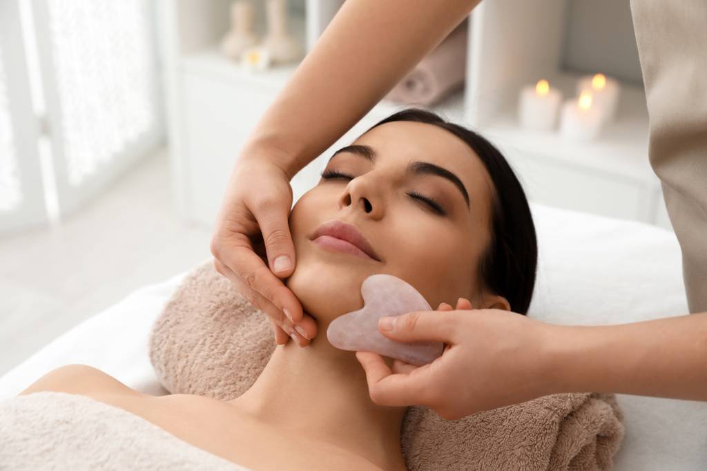 Rosenquarz-Roller-Test: Eine Frau liegt auf einem Massagetisch und wird im Gesicht mit einem Gua-Sha-Stein behandelt 