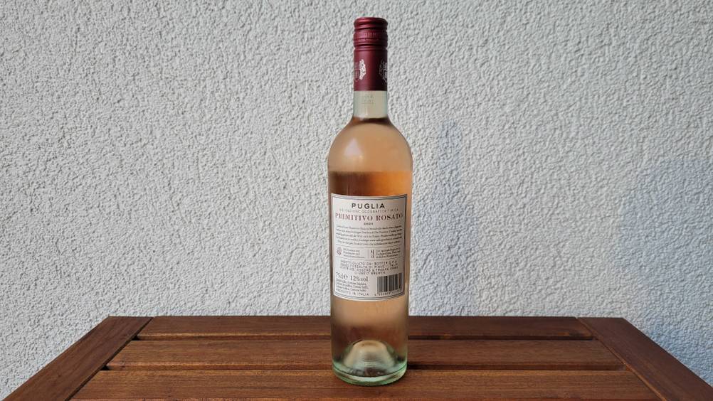 Rückseite einer Flasche des getesteten Roséwein vor einer hellen Wand auf einem Holztisch stehend.