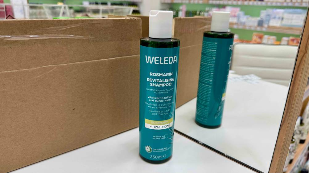 Eine Flasche Rosmarin-Shampoo im Test auf einer hellen Fläche, sie spiegelt sich im Hintergrund.