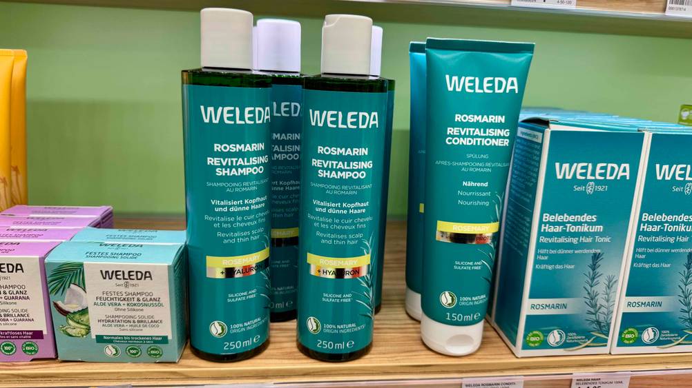 Mehrere Flaschen des Rosmarin-Shampoos auf einem Verkaufsregal neben anderen Produkten.