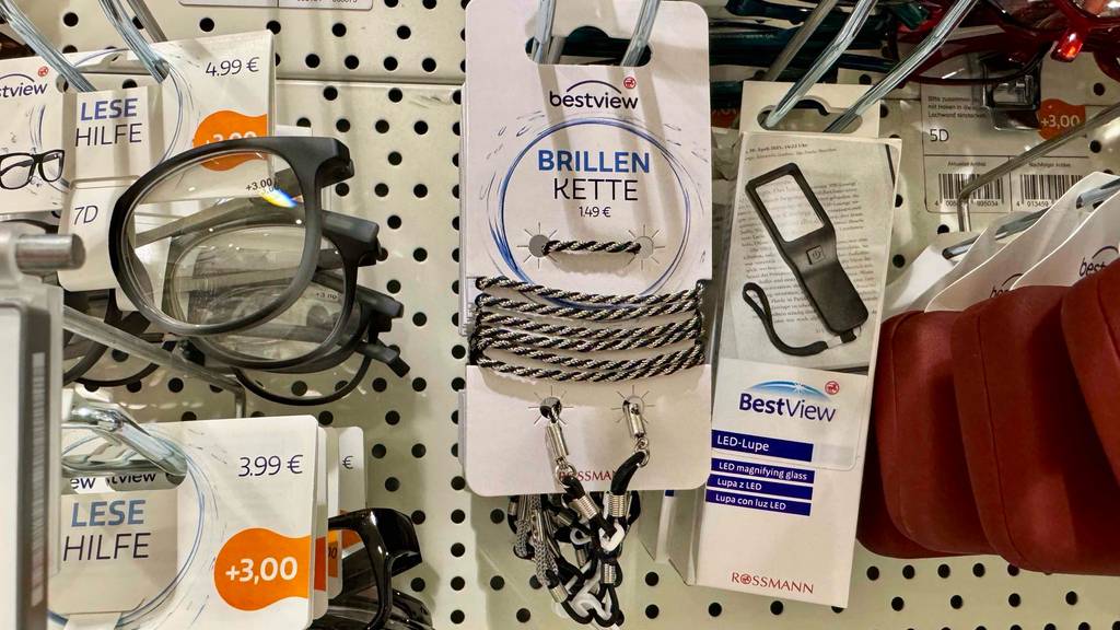 Im Test: Eine Brillenkette aus schwarzer Kordel inklusive Packung hängt neben weiteren Lesehilfen an einem Verkaufsstand.