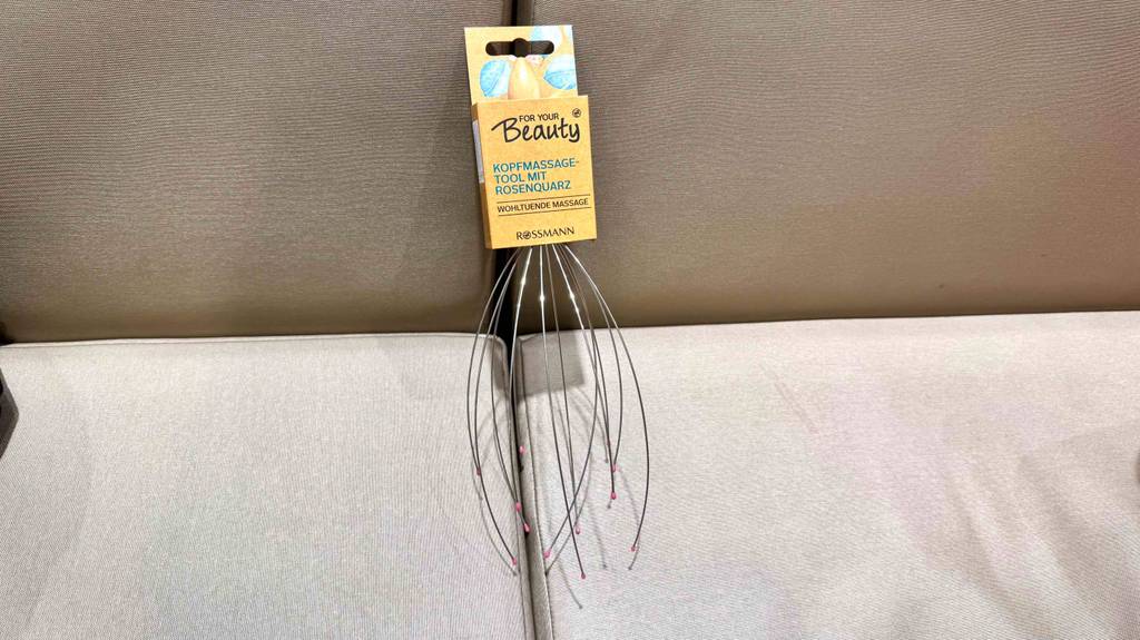 Eine Kopfmassage-Spinne im Test liegt mit Kartonblister auf einer grauen Couch.