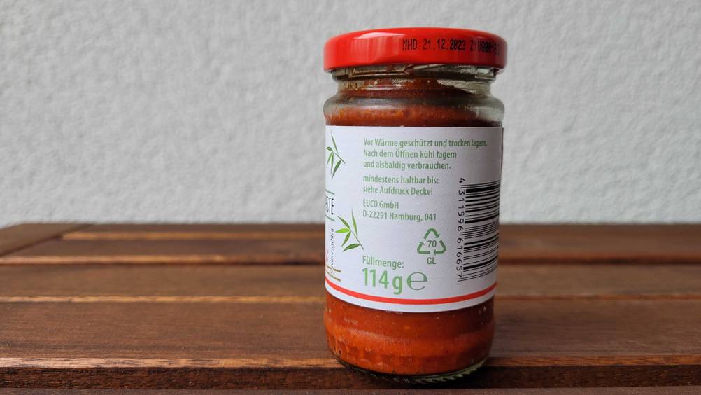 Ein Glas rote Currypaste im Test von der Seite mit Informationen auf einem Holztisch.