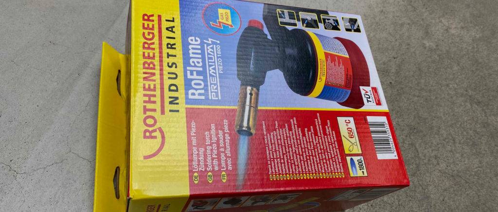 Die Verpackung der getesteten Lötlampe liegt auf einem grauen Untergrund.