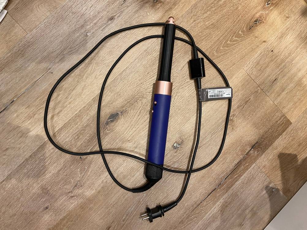 Die getestete rotierende Warmluftbürste liegt mit Ihrem Kabel auf dem Holzboden.