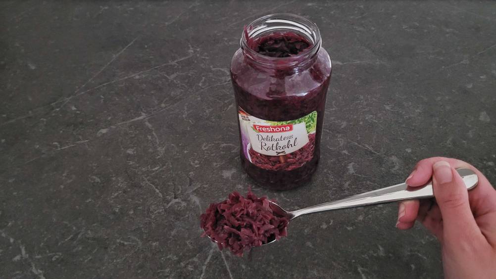 Rotkohl im Test: Auf dem Tisch befindet sich ein Teelöffel Rotkohl vor einem Rotkohl-Glas. 