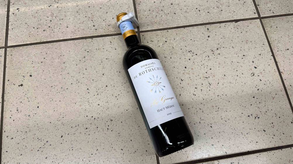 Auf einem Fließenboden liegt eine Flasche des getesteten Rotweins.