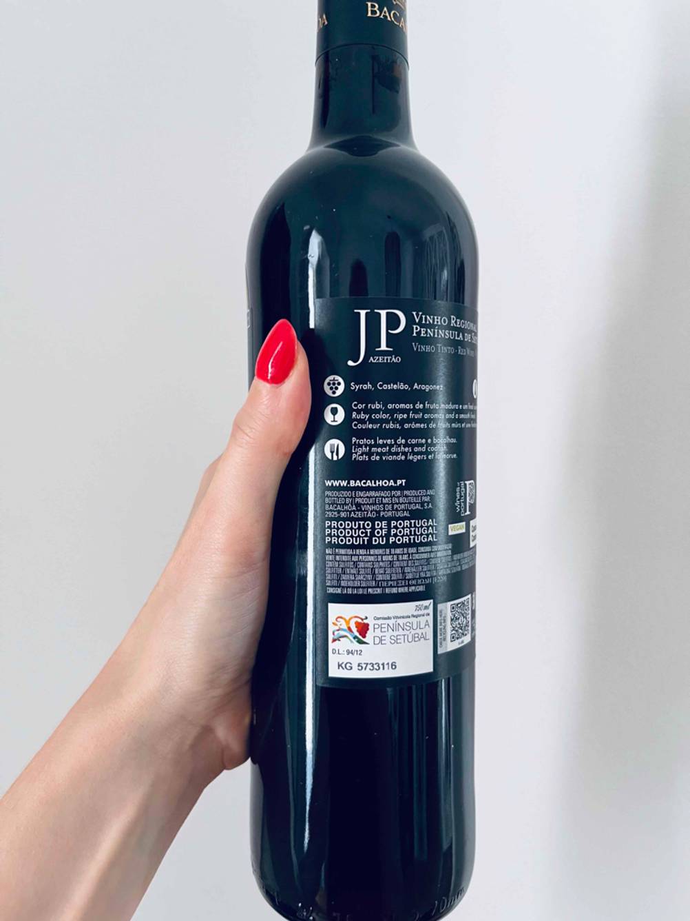 Rückseite einer Flasche getesteten Rotwein (lieblich) von einer Hand vor eine helle Wand gehalten.