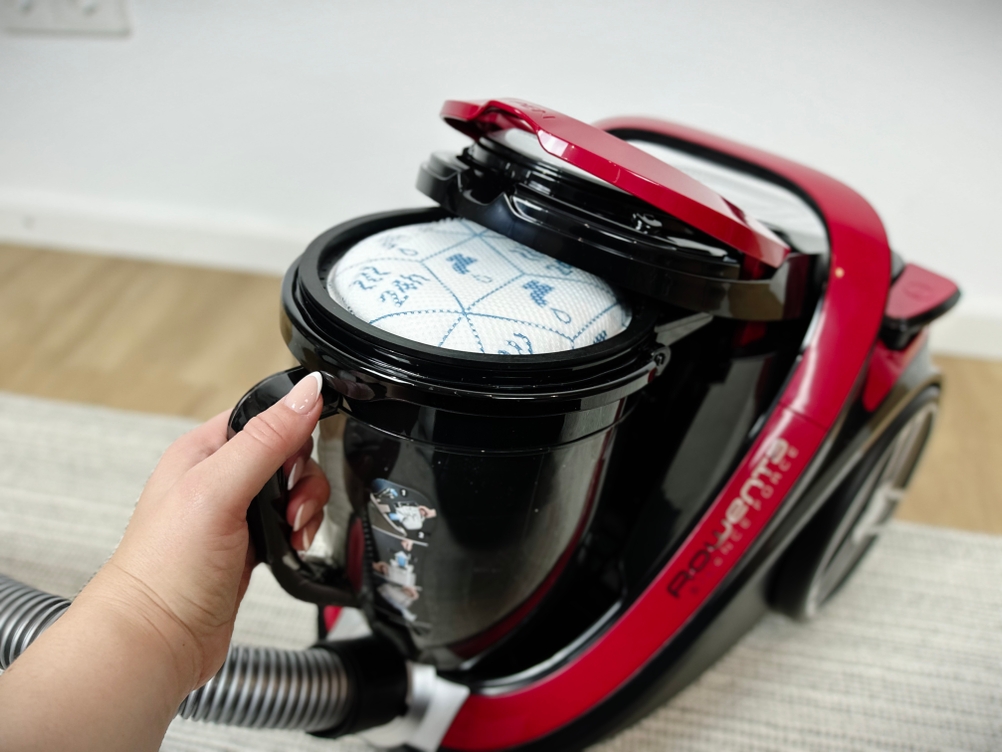 Eine Hand hebt den Staubbehälter mit integriertem Filtereinsatz aus dem Rowenta RO7649EA. Der Filter befindet sich unter dem Deckel.