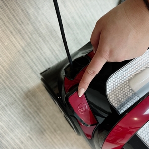 Eine Hand zeigt auf die Kabelaufrolltaste des Rowenta RO7649EA. Die Taste ist rot und deutlich mit einem Steckersymbol markiert.