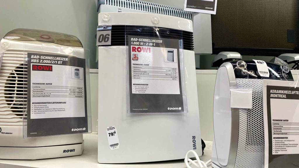 Ein ROWI Bad-Heizstrahler im Test: Ansicht von vorn auf die weiße Kunststoffausführung eines, im Verkauf neben anderen Bad-Schnellheizern inklusive Produktinformationen, ausgestellten Modells.