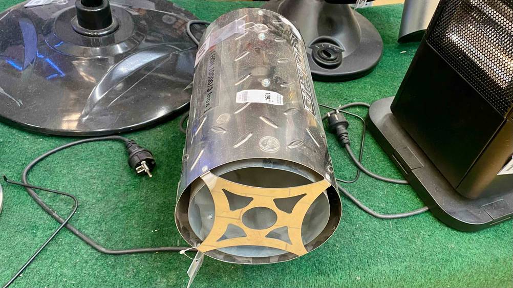 Gasheizstrahler-Test: ein Gasheizstrahler in Form eines Zylinders aus Metall inklusive schwarzem Kabel liegt inmitten anderer Heizstrahler auf einem grünen Kunstrasen im Verkaufsbereich.