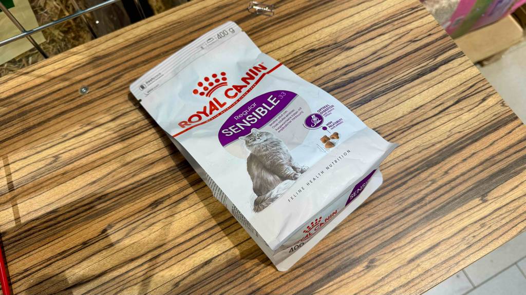 Eine Packung Katzenfutter sensitive liegt zum testen auf einem Holzregal.