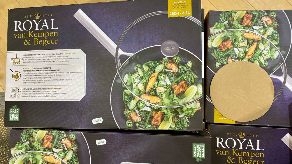 Mehrere Verpackungen übereinander mit Woks inklusive Glas-Deckel stehen zum Test bereit.