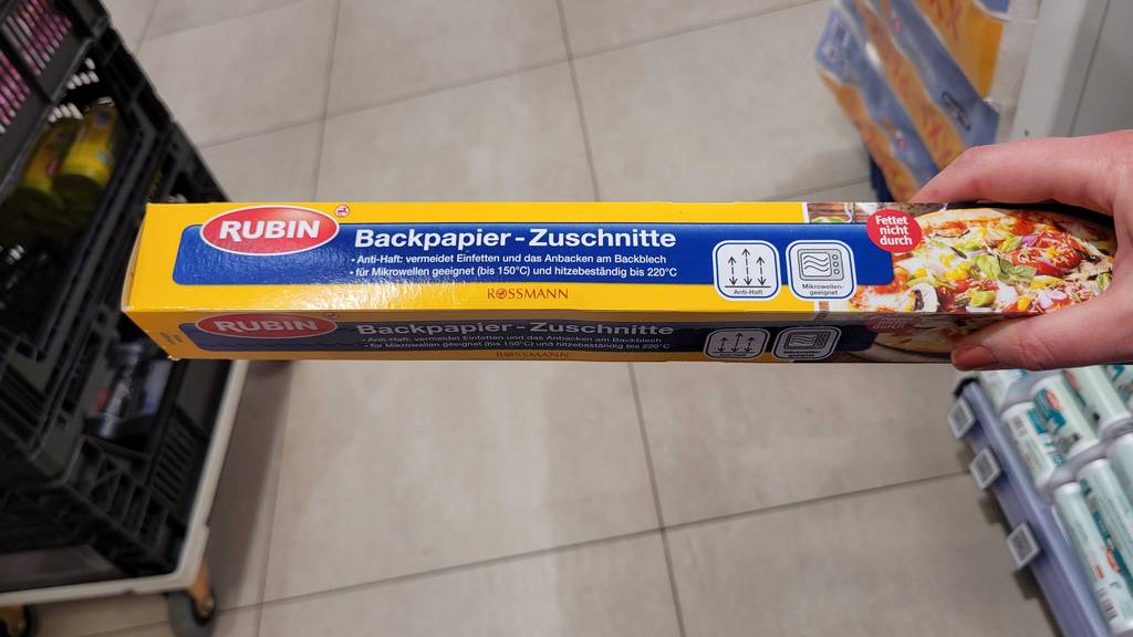 Getestetes Backpapier mit Zuschnitten in einer Packung von Rubin, von einer Hand im Geschäft gehalten.
