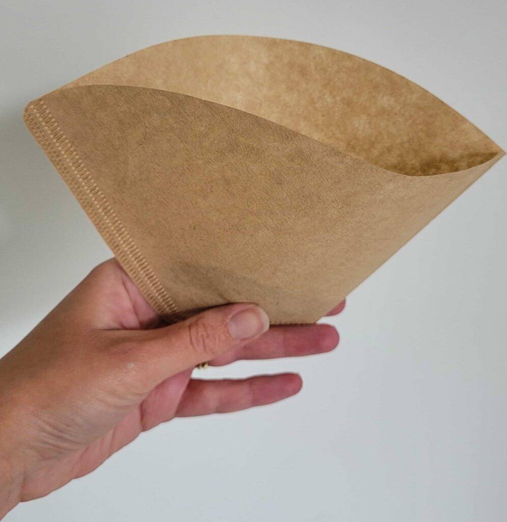 Eine Hand hält einen getesteten Kaffeefilter in Braun vor ein er weißen Wand.