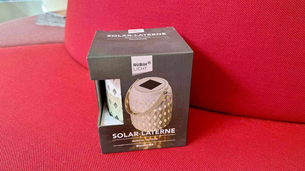 Im Test: Eine Solar-Laterne steht in ihrer Originalverpackung auf einem roten Unter- und Hintergrund.