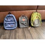 Drei Rucksäcke stehen nebeneinander auf einem gefliesten Boden