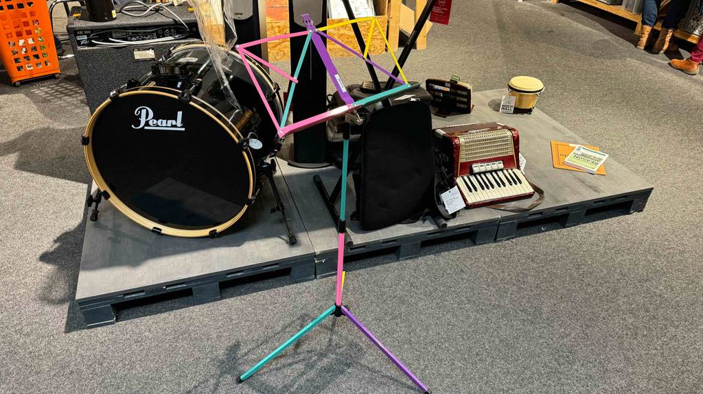 Notenständer-Test: ein mehrfarbiges Modell steht aufgebaut vor diversen Musikinstrumenten in einem Verkaufsbereich.
