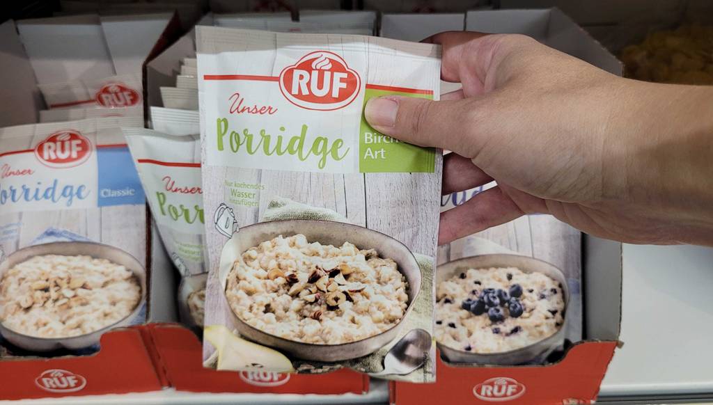 Hand greift nach einer Packung Instant-Oats von Ruf im Test, mit Porridge der Geschmacksrichtung Bircher Art.