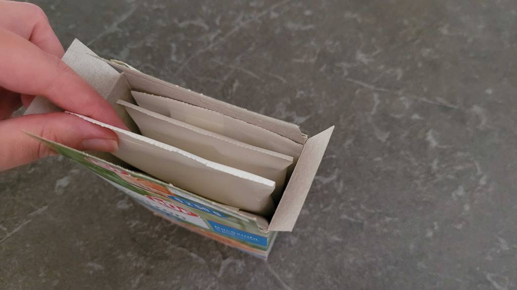Eine Hand zieht aus der Verpackung einen Beutel mit Natron gefüllt raus.