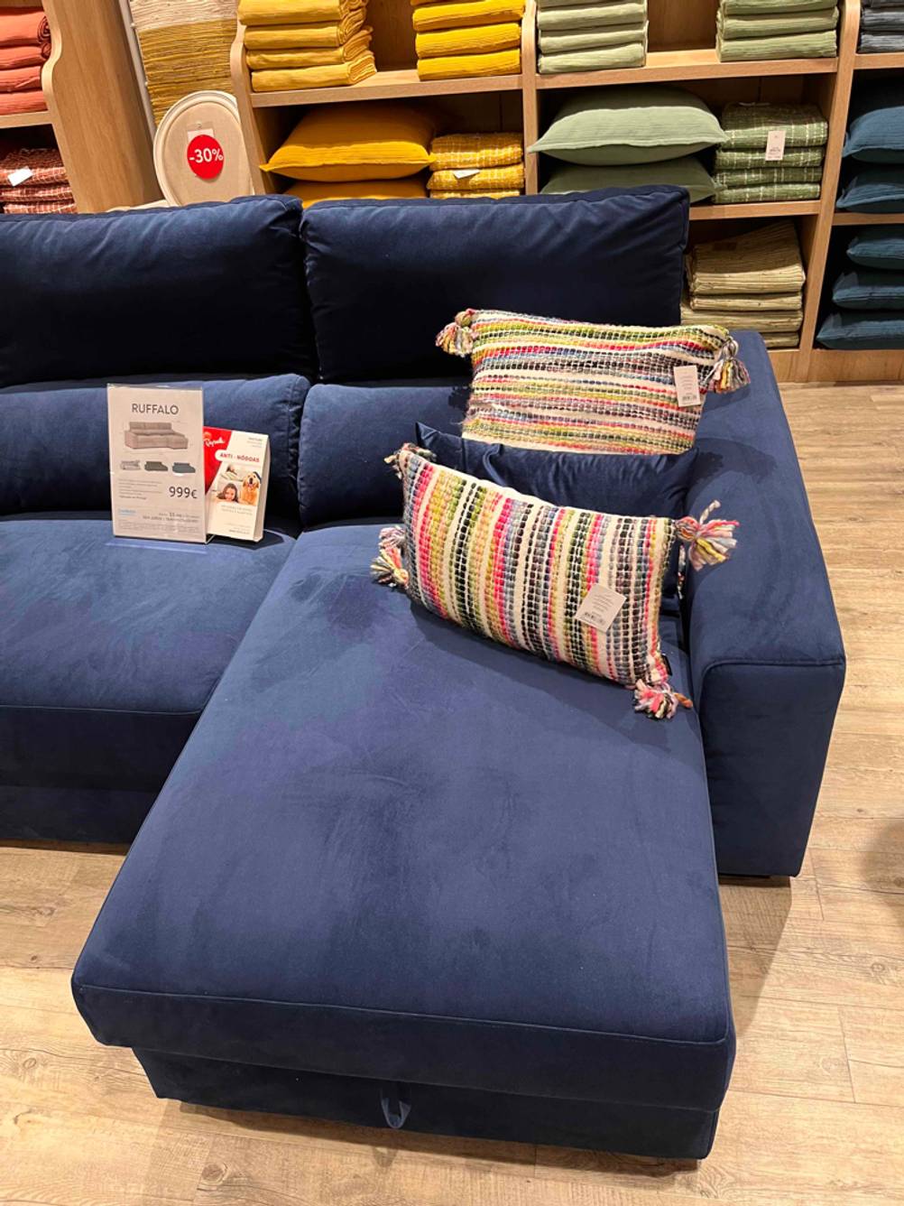 Integrierte Chaiselongue inklusive bunten Kissen eines Relaxsofas im Test: Ansicht von vorn auf das blaue Sofa in einem Ausstellungsbereich.
