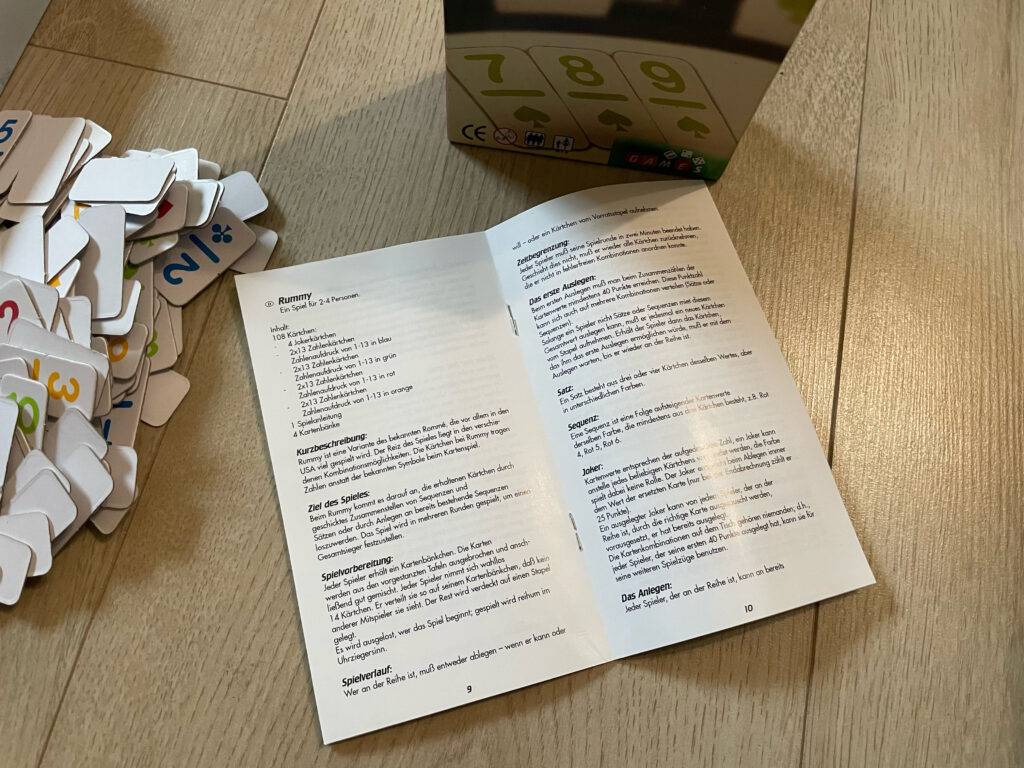 Rummy-Test: Die aufgeschlagene Anleitung liegt zwischen Spielkarton und Spielkarten.