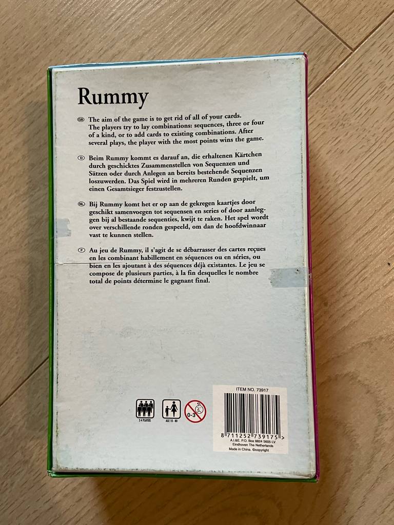 Rummy im Test: Der Spielkarton liegt mit der Rückseite nach oben auf einem Holztisch.